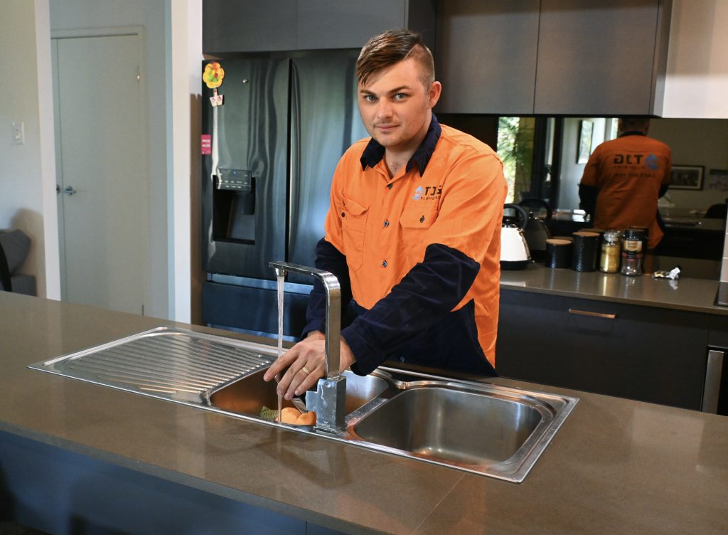 handsome plumber installing kitchen mixer in home