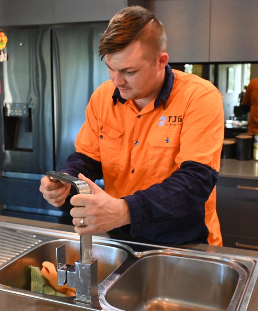 handsome plumber installing kitchen mixer in home